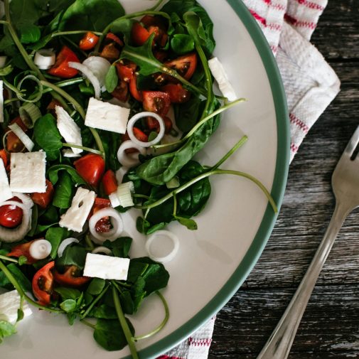A vibrant and colorful spinach salad with feta cheese and tomatoes on a rustic table.